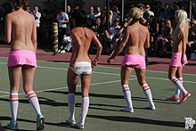 Topless female players in short skirts and socks on public court.